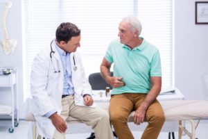 Senior man showing stomach ache pain to doctor